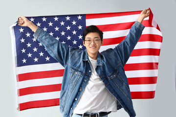 Young Asian man with USA flag on light background