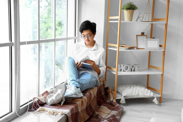 Young Asian man reading book on his day off at home