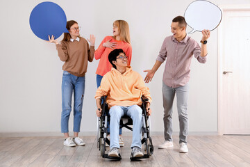 Group of teenagers with boy in wheelchair and speech bubbles near light wall