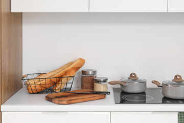 White kitchen counters with cutting board, electric stove, cooking pots and utensils