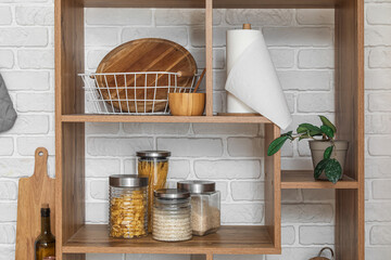 Wooden shelving unit with cutting boards and utensils near white brick wall