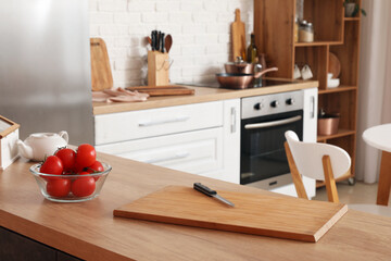 Wooden cutting board with knife and fresh tomatoes on table in modern kitchen