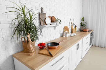 Wooden counter with cutting boards, houseplant, mannequin and frying pan in modern kitchen