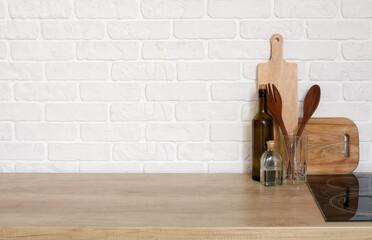 Wooden countertop with cutting boards and utensils near white brick wall