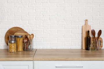 Wooden countertop with cutting boards and utensils near white brick wall