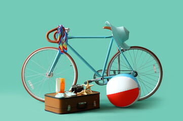 Bicycle with suitcase, camera and beach accessories on turquoise background. Travel concept