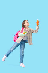 Happy little girl with bottle of juice and lunchbox on blue background