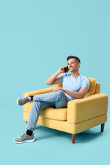 Handsome man talking by mobile phone in yellow armchair on blue background