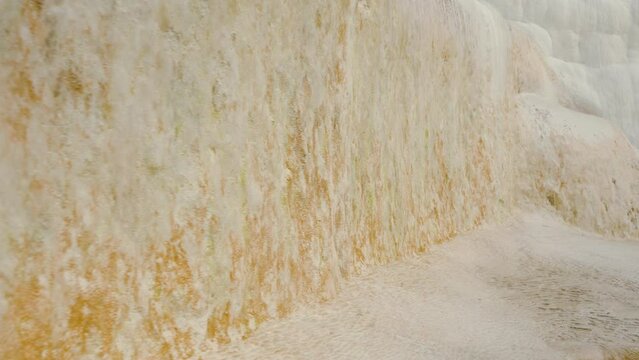 A young woman stands at the edge of a natural pool with a backdrop of white travertine rock. A unique location in Pamukkale.