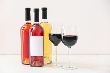 Bottles and glasses of different exquisite wine on light background