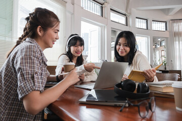 A group of cheerful Asian college students are enjoying talking and discussing their group project while sitting in a coffee shop together.