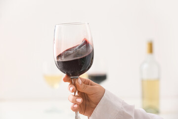 Female hand with glass of exquisite red wine on light background, closeup