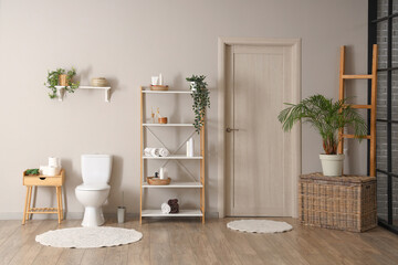 Interior of modern restroom with toilet bowl and shelving unit