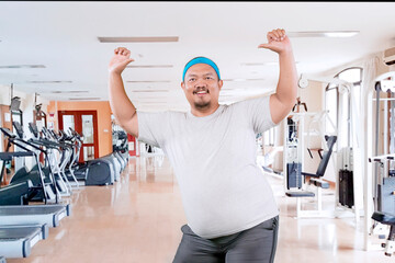 funny fat Asian man in white t-shirt smiling and dancing happily in a gym