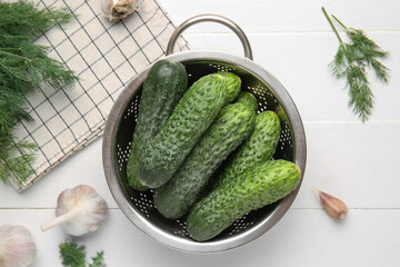 Colander with fresh cucumbers, garlic and dill on white wooden background