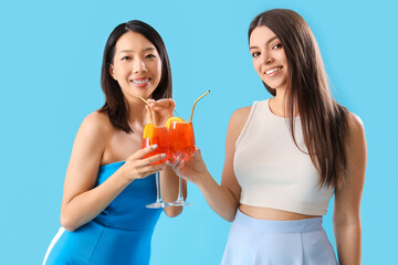 Beautiful young women with glasses of tasty aperol spritz cocktail on blue background