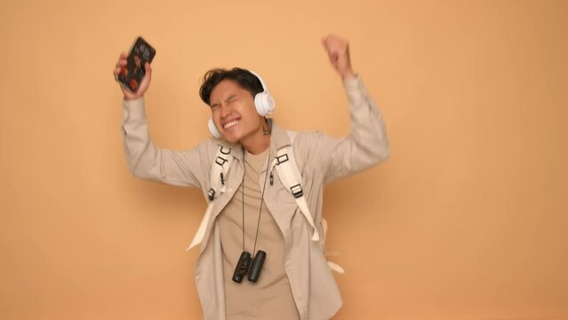 Young handsome Asian man listening to music with headphones and mobile phone against orange background