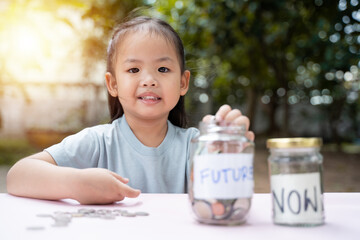 Little Asian girl saving money in Future bottle and now bottle , learning about saving, Kid save money for the future. Money, finances, insurance, and people concept. - 661279214