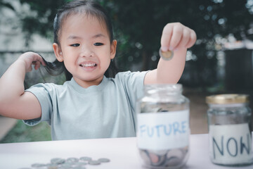 Little Asian girl saving money in Future bottle and now bottle , learning about saving, Kid save money for the future. Money, finances, insurance, and people concept. - 661279218