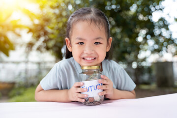 Little Asian girl saving money in Future bottle and now bottle , learning about saving, Kid save money for the future. Money, finances, insurance, and people concept. - 661279221