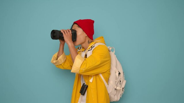 Portrait of Asian woman in yellow raincoat and red hat with camera on blue background