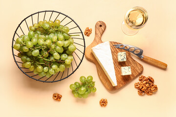 Wooden board with tasty cheese, grapes, nuts and glass of wine on beige background