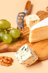 Wooden board with tasty cheese on beige background