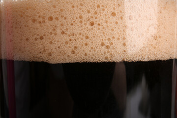 Glass of dark beer with foam as background