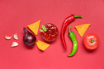 Bowl with tasty salsa sauce, ingredients and nachos on red background