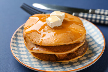 Plate with tasty pumpkin pancakes and pieces of butter on blue background
