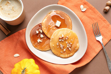 Plate of tasty pumpkin pancakes with piece of butter, honey and nuts on brown background
