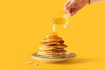 Woman pouring sweet honey onto tasty pumpkin pancakes on yellow background - obrazy, fototapety, plakaty