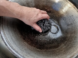 Young housewife woman holding cleaning sponge scrub and washing the dirty frying pan with a pattern of grease and oil stains.

 