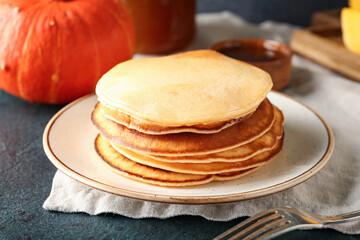 Plate with tasty pumpkin pancakes on dark background