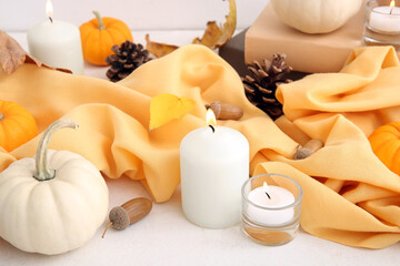 Fototapeta na wymiar Burning candles with scarf, pumpkins, autumn leaves and acorns on white background