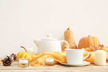 Burning candles with cup of tea, scarf, pine cone, pumpkins and autumn leaves on table against...