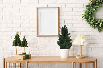 Wooden table with small Christmas tree, gift box and lamp near white brick wall
