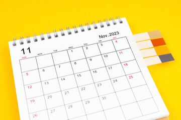The November 2023 Monthly desk calendar and blank adhesive note on yellow background.
