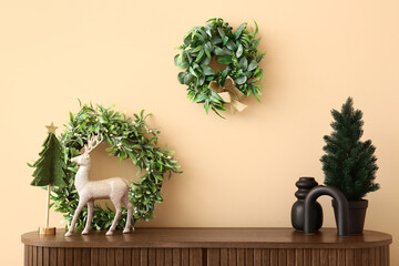 Wooden cabinet with small Christmas trees, deer and wreathes near beige wall