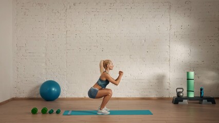 Healthcare creative advertisement concept. Woman fitness coach in the room doing squats side view.
