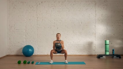 Healthcare creative advertisement concept. Woman fitness coach in the room doing deep squat with kettlebell.