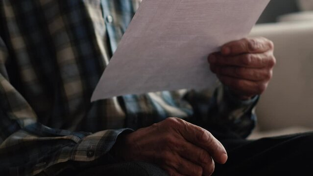 Any paper requires attention. An interested elderly man draws up documents and reads documents. Concentrated man thinking about signing an agreement. Close-up.