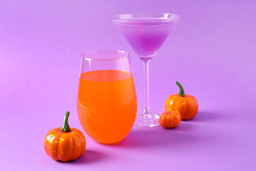 Glasses of delicious cocktails with pumpkins for Halloween celebration on purple background