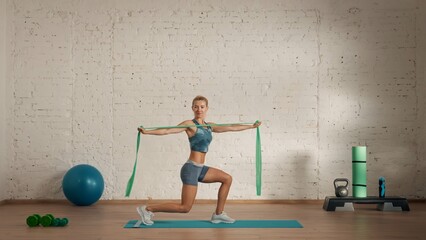Healthcare creative advertisement concept. Woman fitness coach in the room doing lunges with rubber band.
