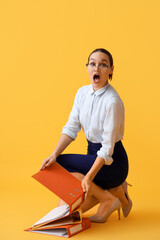 Shocked young businesswoman with document folders on yellow background