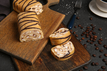Wooden boards with sweet cut sponge cake roll on black background