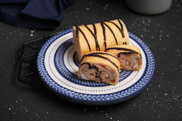 Plate with sweet sponge cake roll and cut pieces on black background