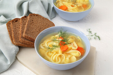 Bowl of tasty chicken soup and bread on white background