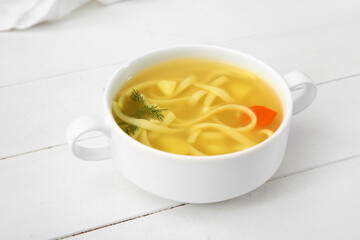 Pot of tasty chicken soup on white wooden background