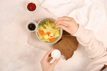 Woman adding salt into bowl with tasty chicken soup on white background